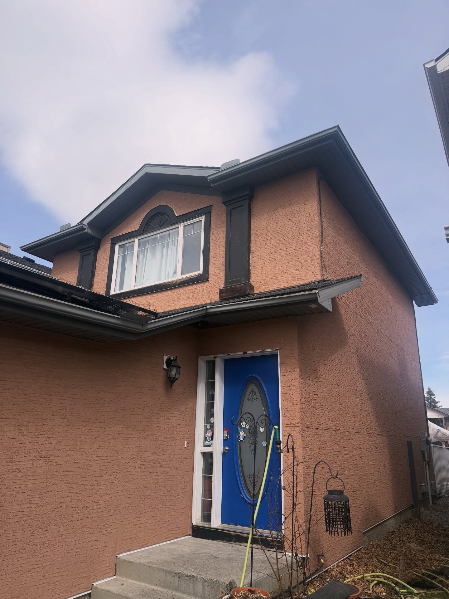 The same Calgary house after re-stucco with a warm textured finish, dark trim and blue front door