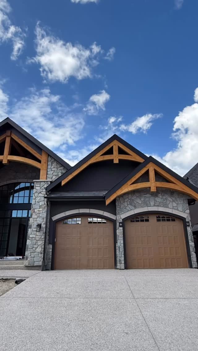 Craftsman-style home with dark stucco, stone garage surrounds and timber gable accents