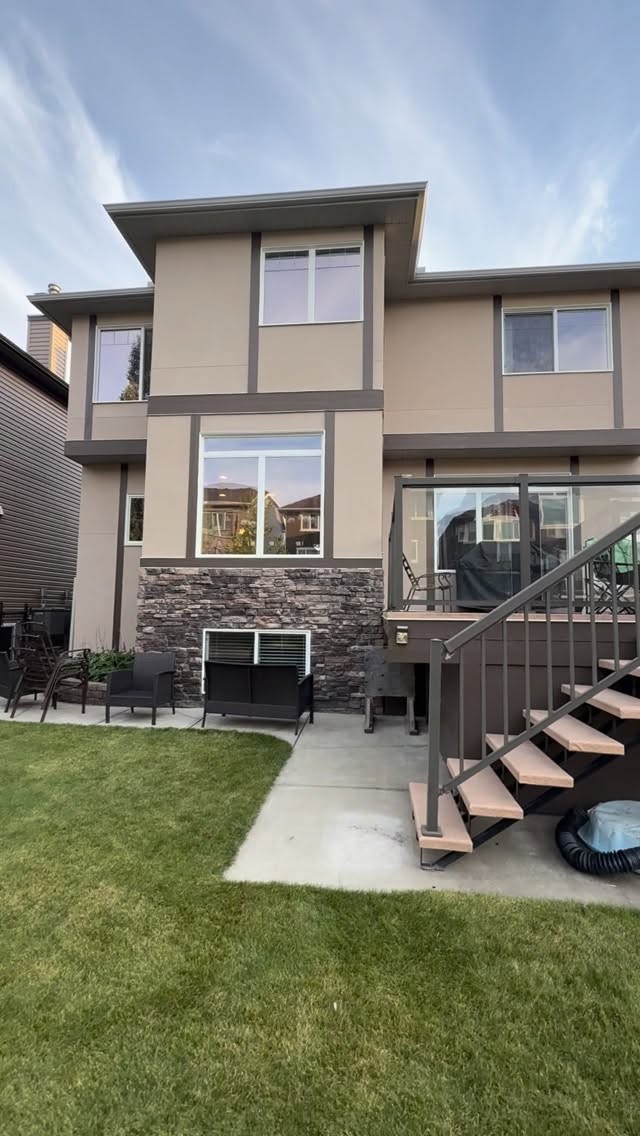 Two-storey home with neutral stucco, stone veneer foundation and backyard steps