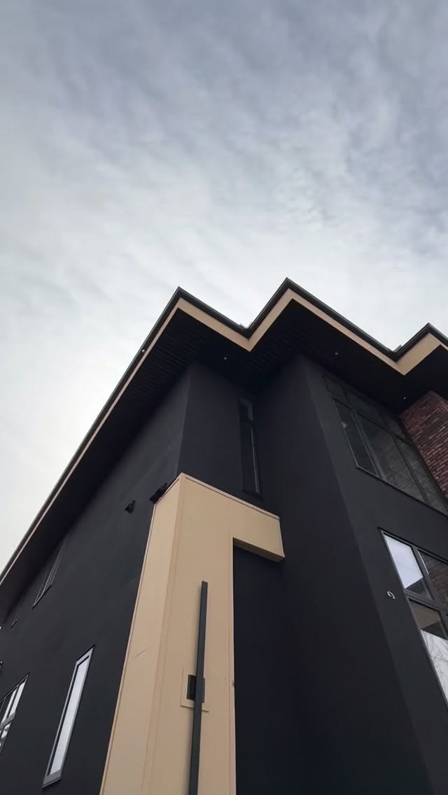 Dark smooth stucco exterior detail beneath angular rooflines with contrasting light trim