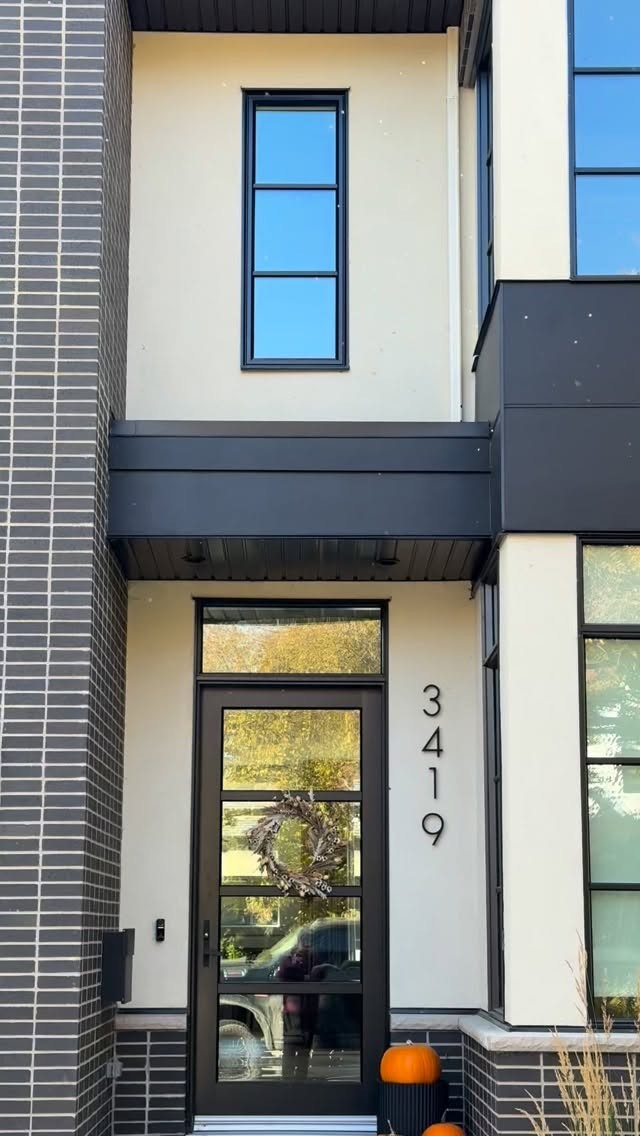 Close-up of smooth stucco entrance with black door trim and dark brick detailing