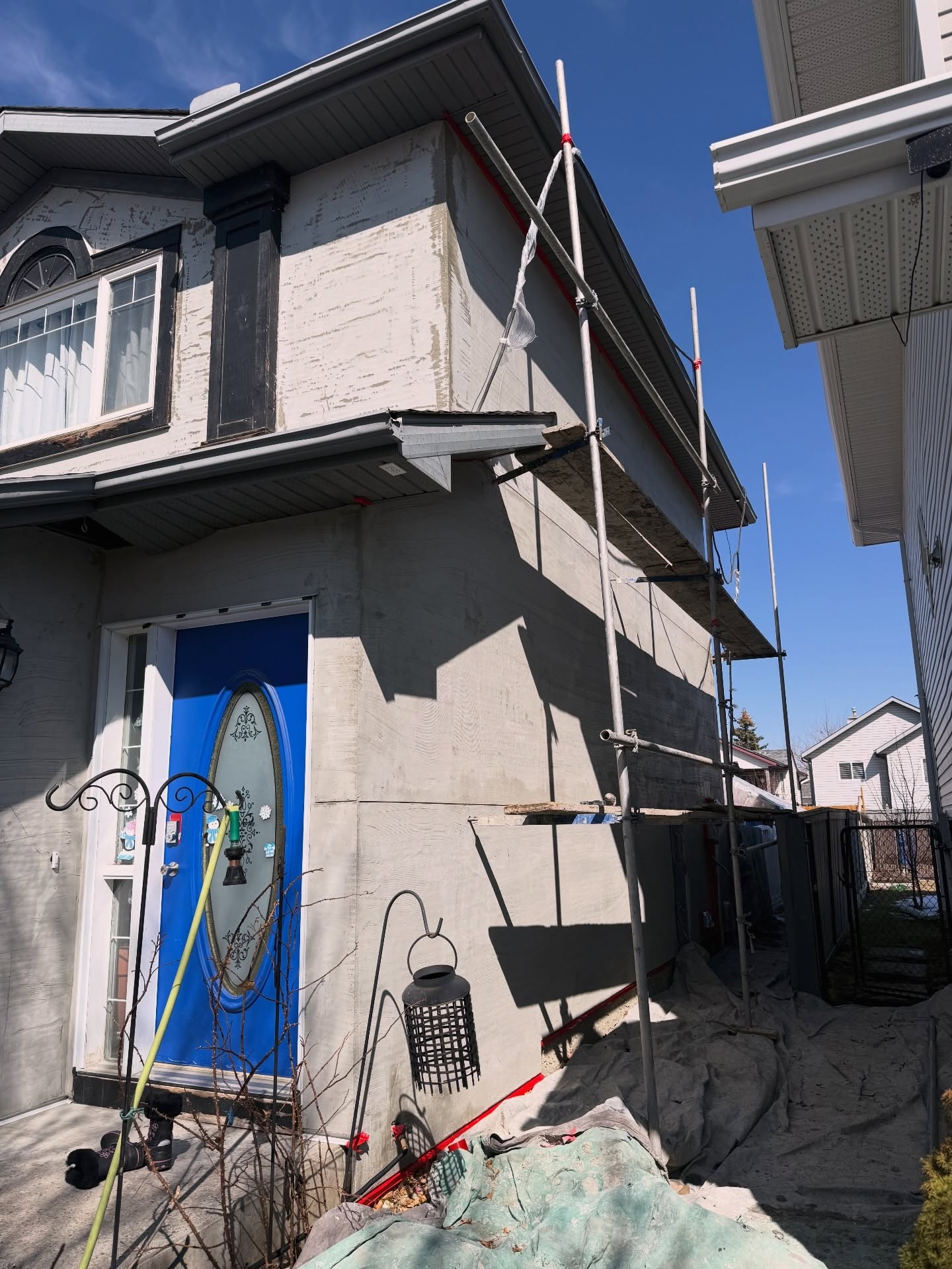 Calgary house before re-stucco with exposed base coat, scaffolding and a blue front door
